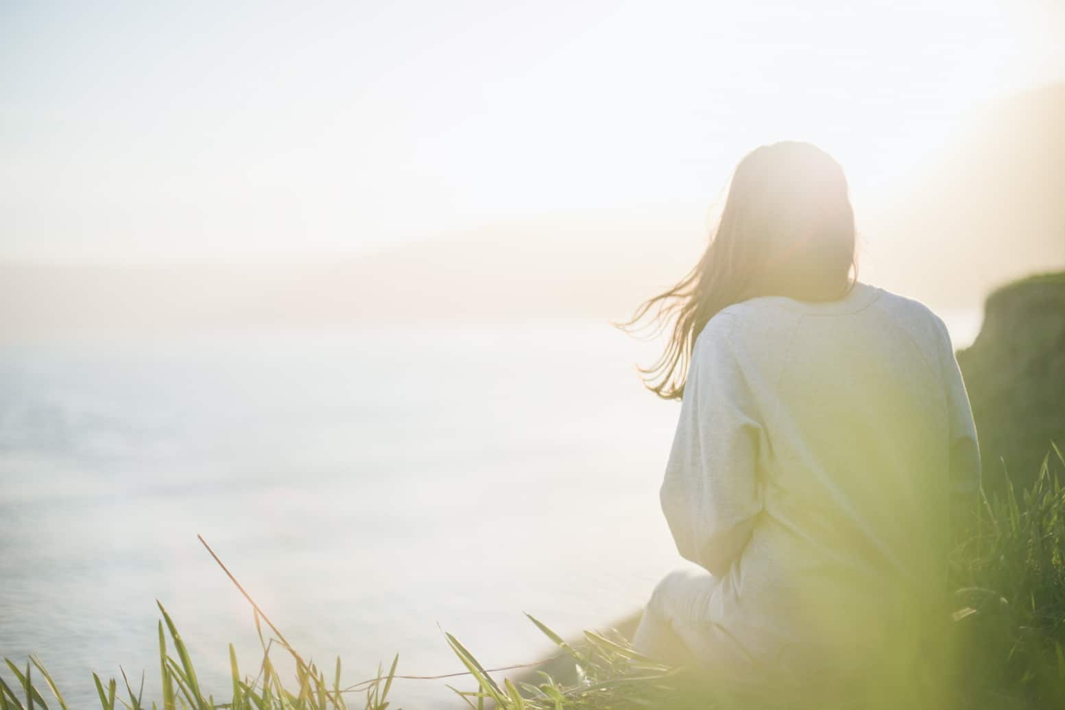 Person looking out toward the sunlit sea, reflecting wellbeing and a sustainable work environment